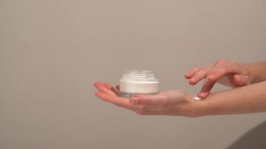 Dişi eller cam maket kavanozundan kremi alır ve bej izole arkaplana sürterek cilde sürerler. Cilt temizleme ve günlük kullanım için nemlendirici krem içeren cilt bakımı.