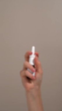 Dikey videoda kadın elinde cam burun spreyi şişesi ve bej arka planda püskürtücü var. Doğal rahatlama, alerji, rhinitis, konfor ve sağlık için solunum bakımı kavramı