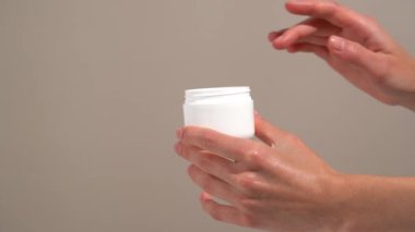 Kadının eli, bej izole edilmiş arka planda parmağı olan beyaz bir model kavanozundan krem topluyor. Besleyici yüz kremi kavramı cilt rahatlığı, denge ve ipeksi yumuşak doku..