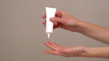 Kadının elleri, beyaz model tüpten serumu parmağına uyguluyor ve bej rengi izole arka planda cildine sürtüyor. Cilt sağlamlığı, ince çizgi indirgenmesi ve gençlik için yaşlanma önleyici serum kavramı