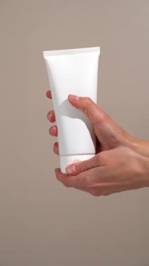 Beyaz model tüp açan ve bej arka plandaki avuç içlerine jel kremi süren kadınların dikey videosu. Tazelik, gençleşme ve güzellik ritüeli için nemlendirici krem kavramı