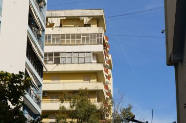 Minimalist formları ve basit balkonları olan güneşli sarı bir ev. Mülk aramaları, şehir merkezli kiralamalar, uzun vadeli yatırımlar ve kentsel Akdeniz konutları için ideal.