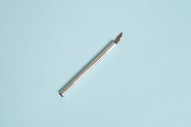 Pastel mavi arka planda gümüş renkli hassas bıçağın minimalist üst görüntüsü. Temiz, düz düz kompozisyon ve yumuşak ışık. İşçiliği, tasarımı, yaratıcılığı, doğruluğu simgeler. Kopyalama alanı.
