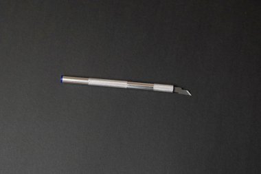 A minimalist flat lay of a silver metal hobby knife on a black textured background. The top-down view and clean studio lighting highlight the precision tool for crafts, design, and modeling.