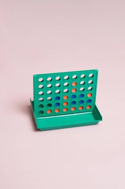 Yeşil tahtası, turuncu ve mavi diskleri olan sıradan dört kişilik bir strateji oyunu. Pastel pembe arka planda minimalist bir stüdyo çekimi. Oyun, mantık, rekabet ve nostalji kavramı.