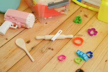 Ahşap zemindeki renkli çocuk oyuncaklarının yüksek açılı görüntüsü. Yaratıcı sanat malzemelerinin dağınık bir koleksiyonu, hamur aletleri ve baloncuk tabanca eğlenceli ve eğlenceli bir ruh halini çağrıştırıyor. Doğal ışık.