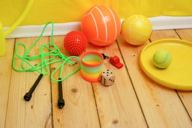 Ahşap zeminde çocuk oyuncakları ve spor aletleriyle dolu renkli bir hayat. Bu canlı çeşitlilikte toplar, bir ip atlama ve ıslık, çocukluk, okul ve aktif oyun çağrıştırıyor..