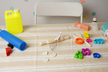 Renkli oyuncak koleksiyonu, pişirme aletleri ve çizgili masa örtüsü üzerindeki nesneler. Yaratıcı oyun, çocukluk aktiviteleri, kaos, dağınıklık ya da düzensizliği öneren parlak bir sahne.