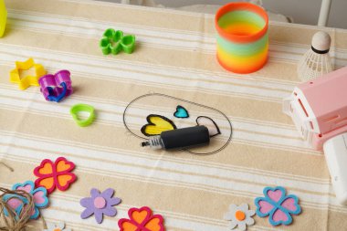 Bir çocuğun yaratıcı çalışma alanının en üst görüntüsü. Gökkuşağı yayı gibi renkli oyuncaklar ve el sanatları malzemeleri çizgili bir kumaşa saçılmıştır. Çocukluk kavramları için parlak, neşeli ve nostaljik bir ruh hali..