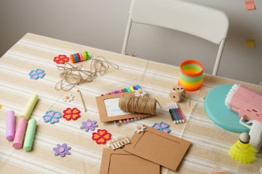 Bir çocuğun renkli sanatlar, el sanatları malzemeleri ve çeşitli oyuncaklarla dolu dağınık aktivite masası. Yaratıcı oyun zamanı, DIY projeleri ve çocukluk eğlencesi sahnesi. Çizgili bir masa örtüsünün üzerindeki doğal ışık..