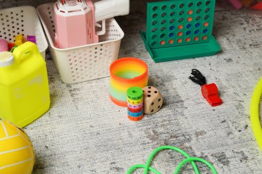 Gri zemine saçılmış renkli çocuk oyuncaklarından oluşan canlı bir koleksiyon. Yüksek açı oyunları, eğitici öğeleri ve gökkuşağı yayını gösterir, neşeli, dağınık ve nostaljik bir hava yaratır..