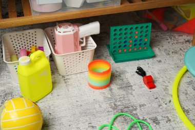 Arka arkaya dört kez oynanan bir oyun, gökkuşağı yayları ve depolama sepetlerinin yanına saçılmış top gibi renkli oyuncaklarla dolu dağınık bir oyun odası zeminine. Işık bile neşeli, nostaljik ve günlük bir hava yaratır..