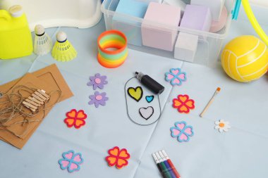 Açık mavi bir yüzeye serilmiş çeşitli yaratıcı oyun parçalarının yüksek açılı görüntüsü. İçinde gökkuşağı oyuncağı, keçeli kalem, boya, spor topları var. Parlak, aydınlatma bile rengarenk paleti vurgular.