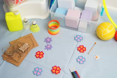 Çocukların yaratıcı projeleri ve oyun zamanları için canlı bir koleksiyon. Açık mavi bir masada sergilenen sanat malzemeleri, spor malzemeleri ve oyuncaklar. Işık bile neşeli bir atmosfer yaratır..