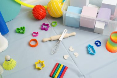 Çocuk oyuncakları ve aktivite ekipmanlarından oluşan canlı bir karışım. Açık mavi bir yüzeyde kil, top, blok ve el işi aletleri modellemeyi içerir. Parlak, aydınlatma bile renkli nesneleri vurgular.