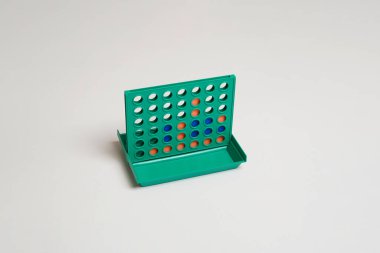 Turuncu ve mavi diskleri yeşil ızgarada olan peş peşe dörtlü bir masa oyunu. Minimalist stüdyo temiz beyaz bir arkaplanda çekilmiş. Strateji, rekabet, mantık ve geçmişe dönük eğlence kavramı.