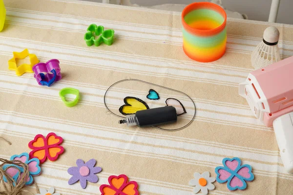 Bir çocuğun yaratıcı çalışma alanının en üst görüntüsü. Gökkuşağı yayı gibi renkli oyuncaklar ve el sanatları malzemeleri çizgili bir kumaşa saçılmıştır. Çocukluk kavramları için parlak, neşeli ve nostaljik bir ruh hali..