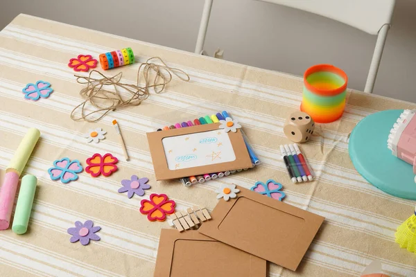 Bir çocuğun yaratıcı çalışma alanına yüksek açılı bir bakış açısı. Masa, bir DIY fotoğraf çerçevesi projesi için keçeli kalem, tebeşir ve keçeli çiçek gibi renkli sanat malzemeleriyle ve çeşitli oyuncaklarla dolu..