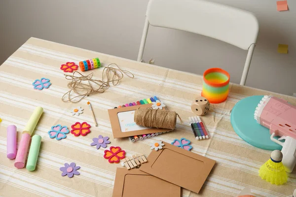 Bir çocuğun renkli sanatlar, el sanatları malzemeleri ve çeşitli oyuncaklarla dolu dağınık aktivite masası. Yaratıcı oyun zamanı, DIY projeleri ve çocukluk eğlencesi sahnesi. Çizgili bir masa örtüsünün üzerindeki doğal ışık..