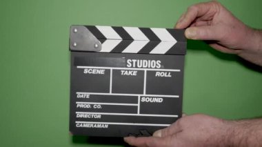 Yeşil arka planda film prodüksiyon alkış tahtası olan eller