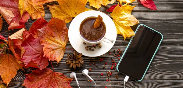 Tasse de café avec des épices cannelle, clous de girofle et poivron rouge. Feuilles d'érable tombées à l'automne et téléphone sur un fond en bois. Image En Vente