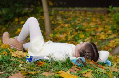 Düşen yaprakların üzerinde yatan ve gülümseyen küçük bir kız. Sonbahar Parkı 'nda parlak sarı, turuncu akçaağaç yaprakları.