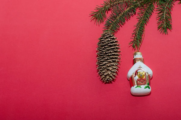 Gałąź choinki z rożkiem i świąteczne dekoracje na czerwonym tle. Minimalistyczna kompozycja, koncepcja uroczystości. — Zdjęcie stockowe