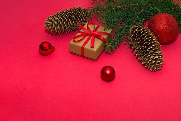 Gałąź choinki z rożkiem i świąteczne dekoracje na czerwonym tle. Minimalistyczna kompozycja, koncepcja uroczystości. — Zdjęcie stockowe
