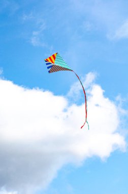 Mavi gökyüzü arka planında beyaz bulutlu çok renkli bir uçurtma. Barışın ve huzurun sembolü.