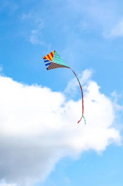 Multi-gekleurde vlieger op een blauwe lucht achtergrond met witte wolken. Symbool van vrede en sereniteit. — Stockfoto