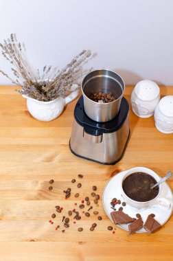 Elektrikli kahve öğütücüsü kahve çekirdeklerini öğütüyor ve masanın üzerinde duruyor, bir fincan sade kahve. Sabah kahve ritüeli.