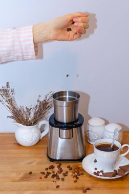 Elektrikli kahve öğütücüsü kahve çekirdeklerini öğütüyor ve masanın üzerinde duruyor, bir fincan sade kahve. Sabah kahve ritüeli.