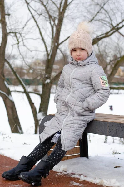 A girl in winter clothes and a hat playing with snow in a winter park. The child is outside during the winter holidays. — Stock Photo, Image