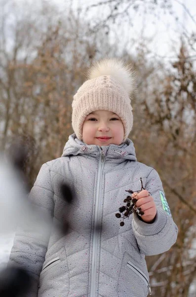 Portrait of a girl in winter clothes and a hat playing with snow in a winter park. The child is outside during the winter holidays. — Stock Photo, Image