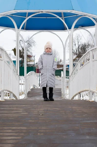 A girl in winter clothes and a hat playing with snow in a winter park. The child is outside during the winter holidays. — Stock Photo, Image