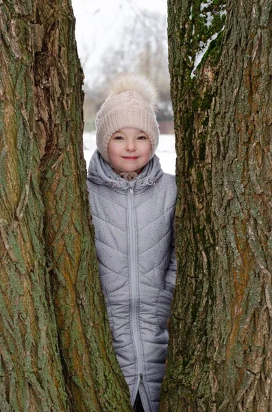 A girl in winter clothes and a hat playing with snow in a winter park. The child is outside during the winter holidays. — Stock Photo, Image