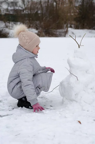 A girl in winter clothes and a hat playing with snow in a winter park. The child is outside during the winter holidays. — Stock Photo, Image