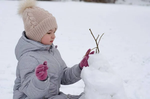A girl in winter clothes and a hat playing with snow in a winter park. The child is outside during the winter holidays. — Stock Photo, Image