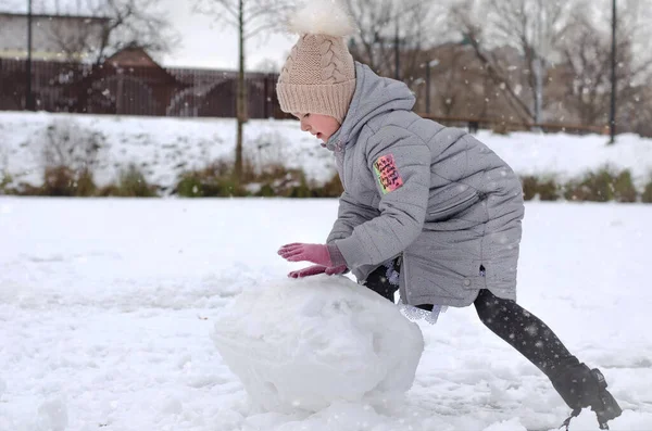 Une fille en vêtements d'hiver et un chapeau jouant avec la neige dans un parc d'hiver. L'enfant est dehors pendant les vacances d'hiver. Images De Stock Libres De Droits