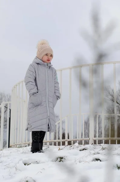 A girl in winter clothes and a hat playing with snow in a winter park. The child is outside during the winter holidays. — Stock Photo, Image