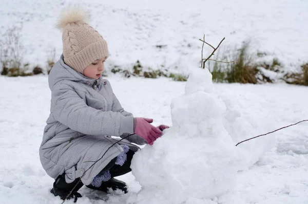 A girl in winter clothes and a hat playing with snow in a winter park. The child is outside during the winter holidays. — Stock Photo, Image