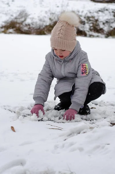 A girl in winter clothes and a hat playing with snow in a winter park. The child is outside during the winter holidays. — Stock Photo, Image