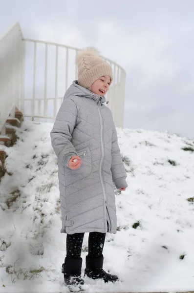 A girl in winter clothes and a hat playing with snow in a winter park. The child is outside during the winter holidays. — Stock Photo, Image