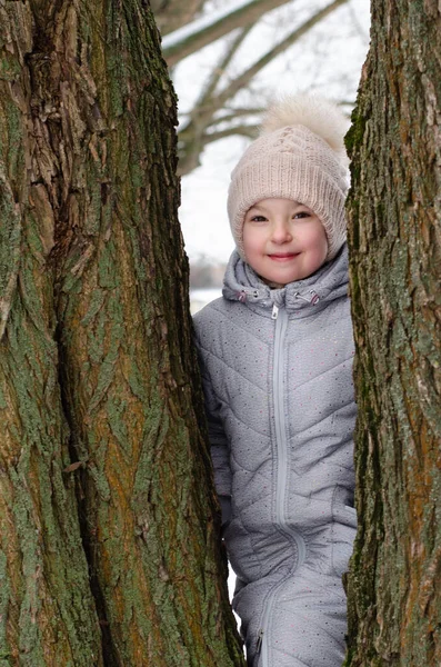 Portrait of a girl in winter clothes and a hat playing with snow in a winter park. The child is outside during the winter holidays. — Stock Photo, Image