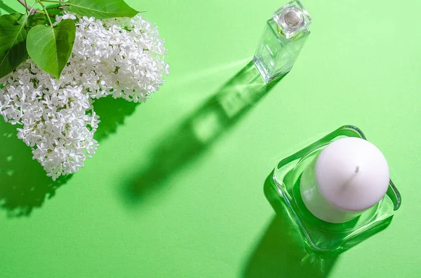 Vita lila blommor, vitt ljus och en flaska med parfym på en grön bakgrund. Ljusa skuggor och ljus. Plats för din text. Stockbild