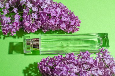 Mor leylak çiçekleri ve yeşil arka planda parfümlü bir şişe. Parlak gölgeler ve ışık. Metnin için yer.