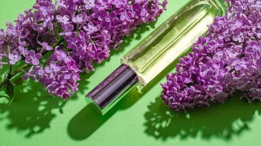 Mor leylak çiçekleri ve yeşil arka planda parfümlü bir şişe. Parlak gölgeler ve ışık. Metnin için yer.