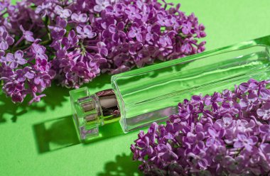 Mor leylak çiçekleri ve yeşil arka planda parfümlü bir şişe. Parlak gölgeler ve ışık. Metnin için yer.