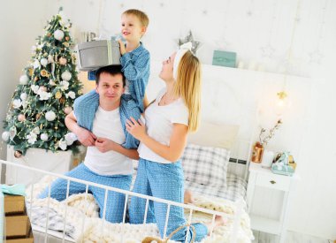 Anne, baba ve küçük oğlu pijamalarıyla bir Noel ağacının arka planında yatıyorlar.