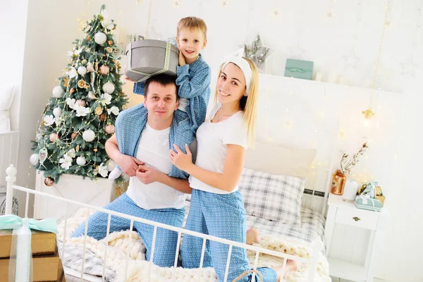 Mamá, papá e hijo pequeño en pijama sentados en la cama contra el fondo de un árbol de Navidad — Foto de Stock